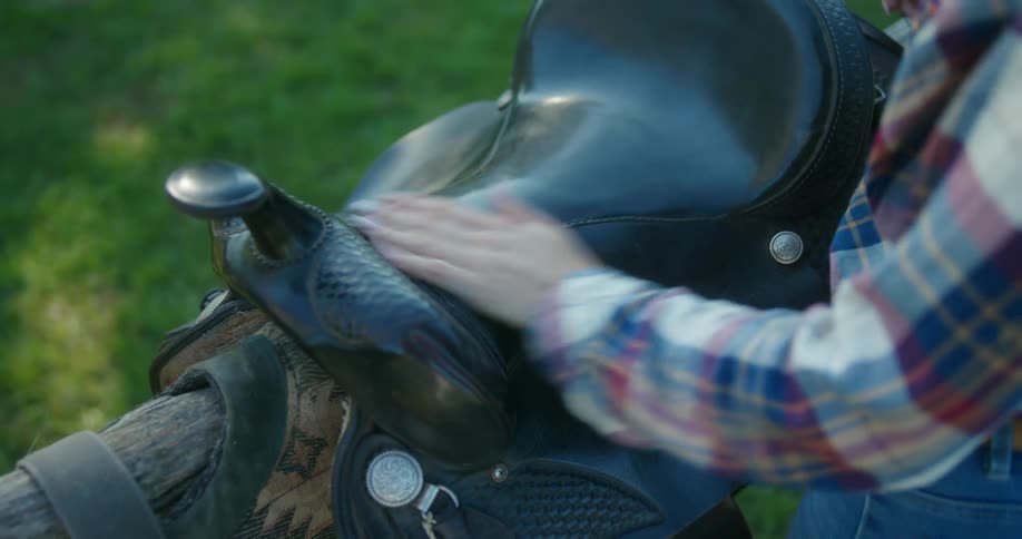 A woman puts a horse saddle on a log and cleans it with her hand