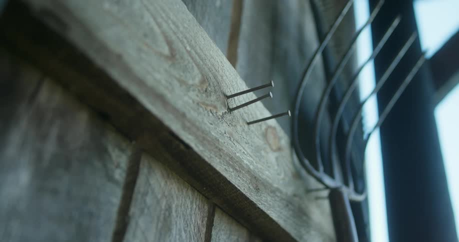 A hand grabs a cowboy off the side of a wood barn than hangs it back up on the nails hammered in beside a pitchfork hung up on the wall