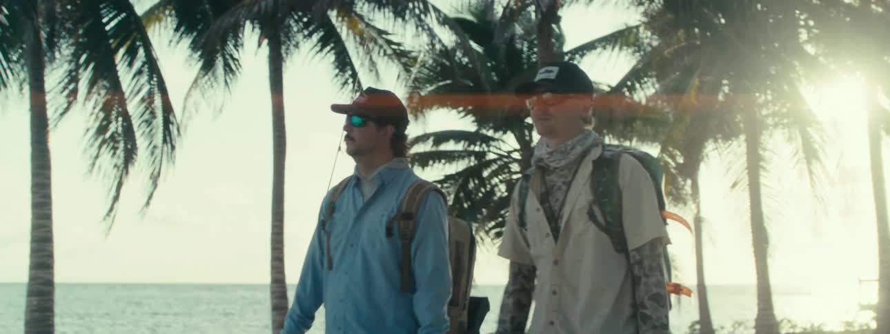 Two men wearing backpacks are walking near a beach in the afternoon