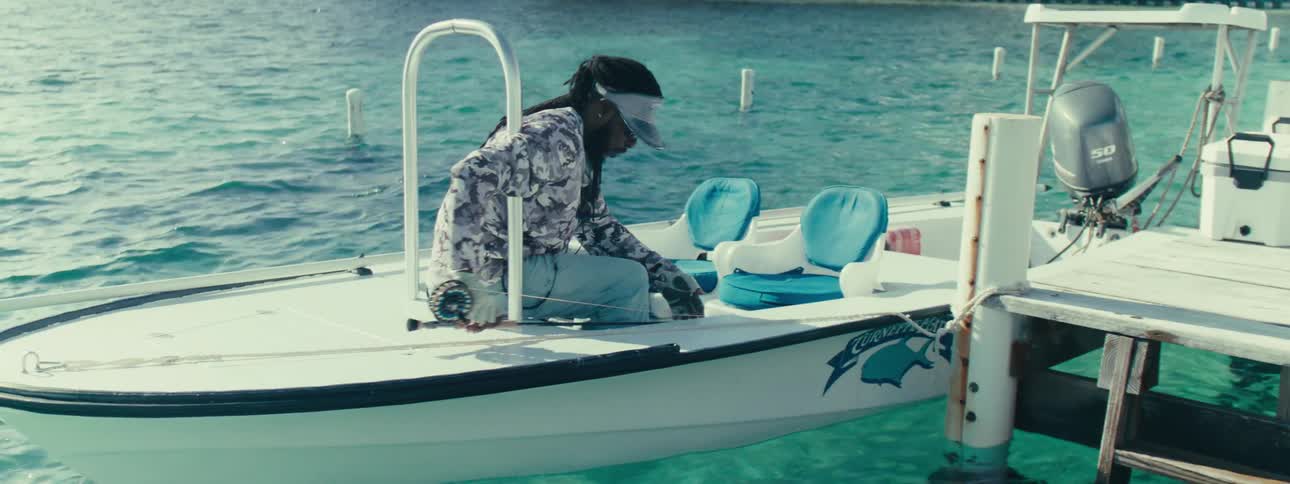 Man handing his colleague who is sitting in a small boat next to the dock a fishing rod