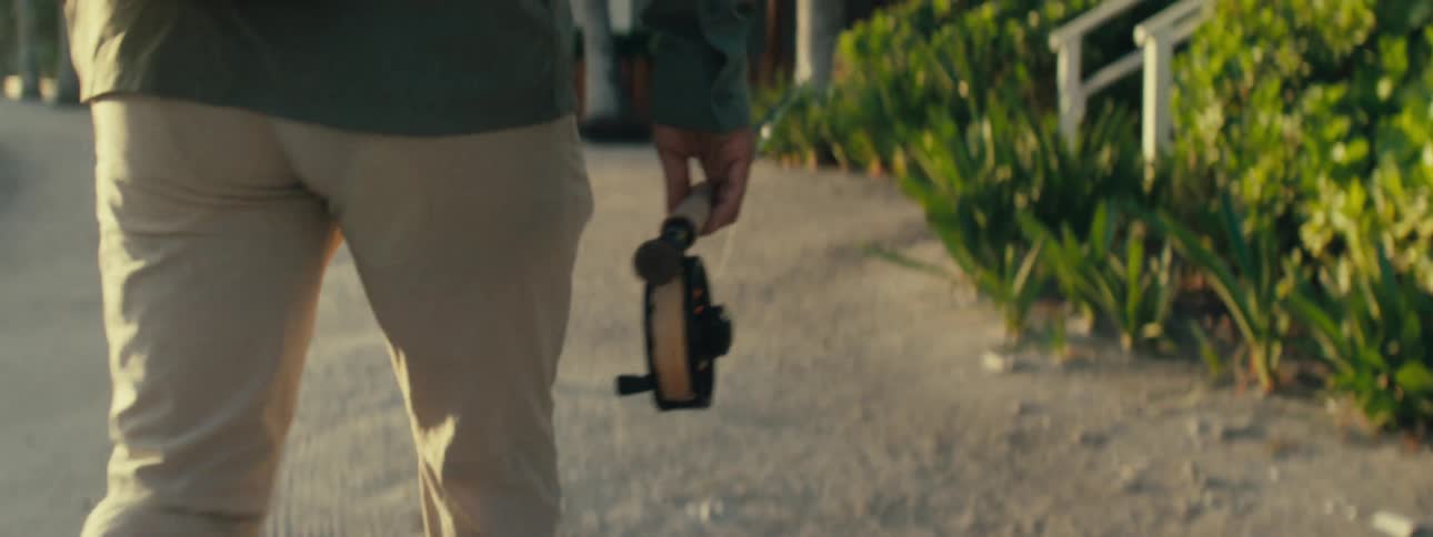 A man is carrying his fishing pole by the shore