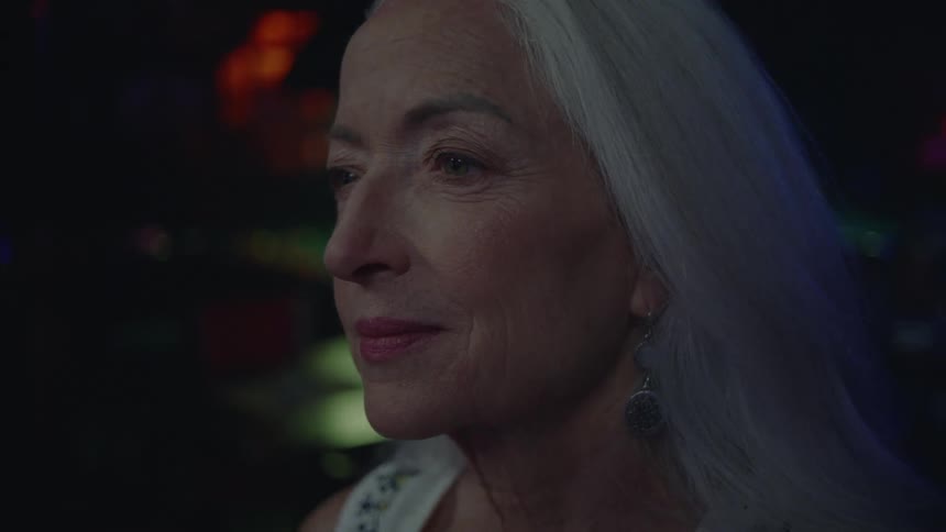 A woman is staring and smiling at something while in a bar with subdued lighting