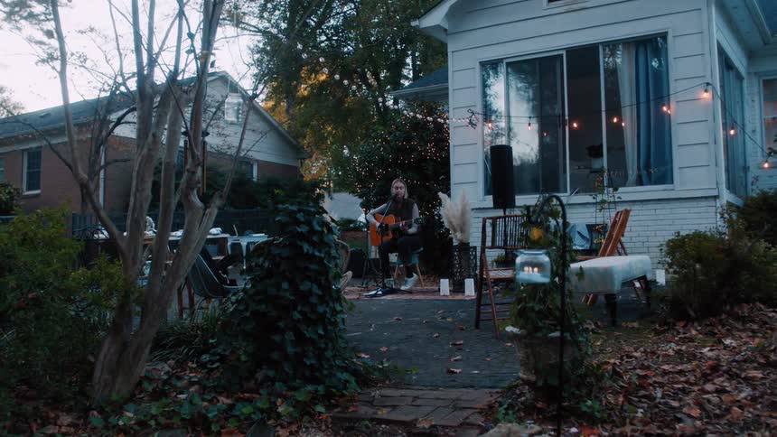 A woman singing in the backyard while playing a guitar