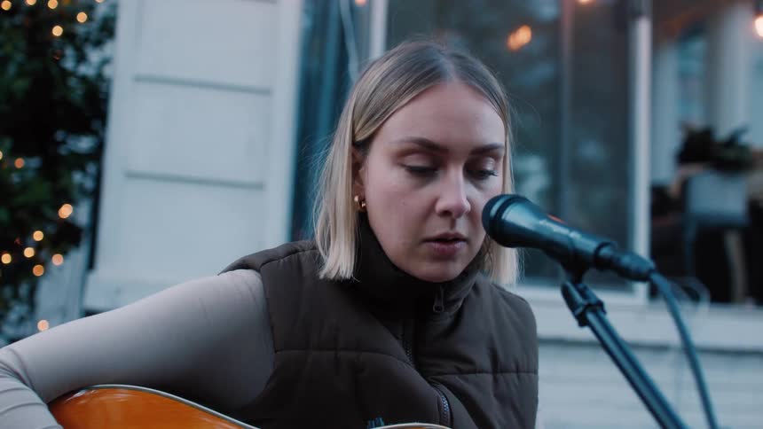 Woman singing and playing the guitar outdoors next to a house
