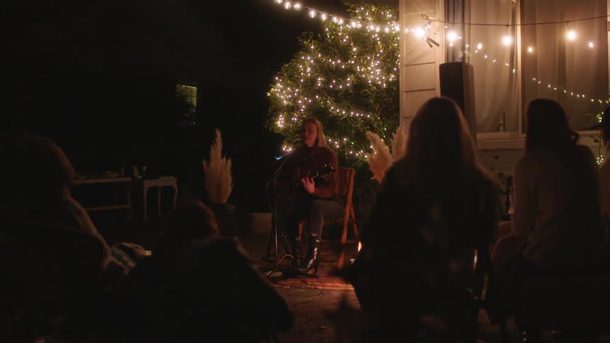 A woman is playing her guitar for people in the yard