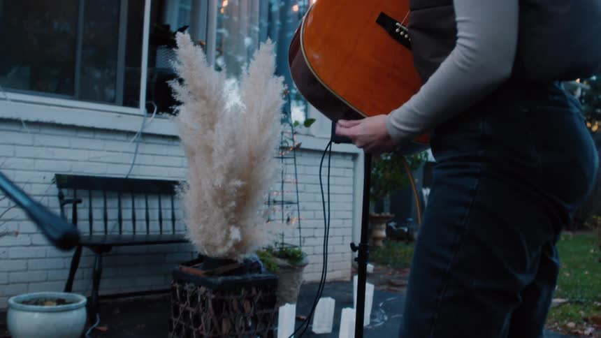 Woman picking up her guitar and connecting it to a wire outdoors