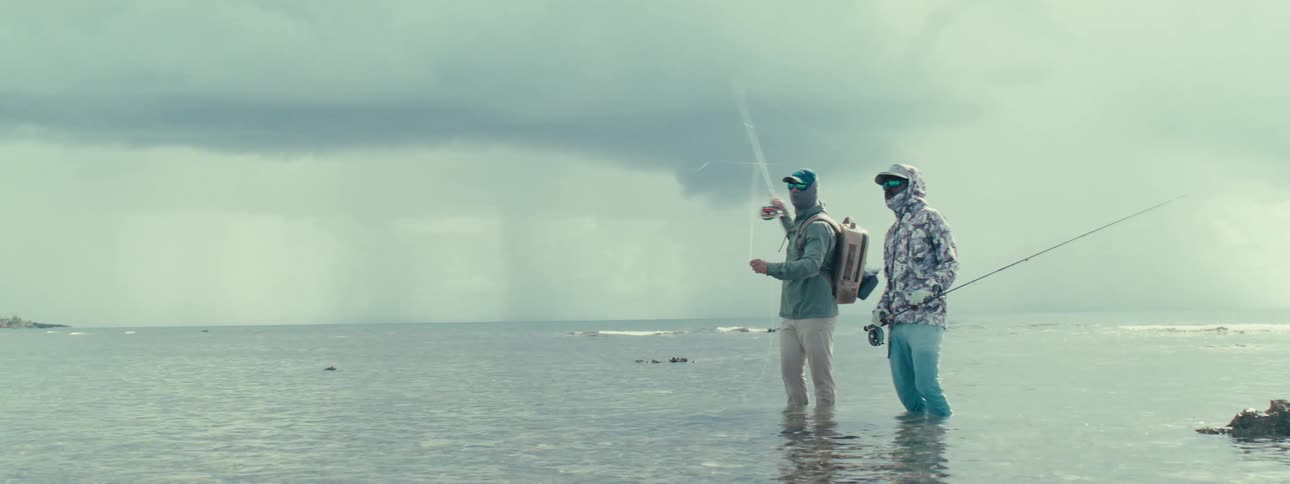 Two men standing in a shallow sea with fishing rods