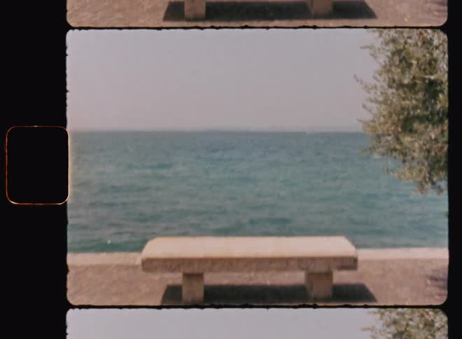 Archival of a cement pebble bench on the wall walkway at the edge of a lake with fast moving water on a sunny day