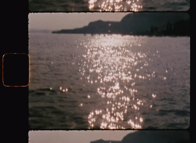 The sun light is shining off of the water and it is shining over the small piece of land that is jutting out into the water