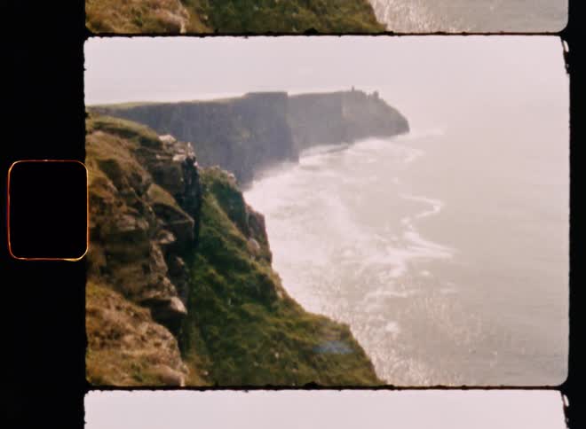 The camera is moving up and down the coast line that is crashing at the base of very steep cliffs