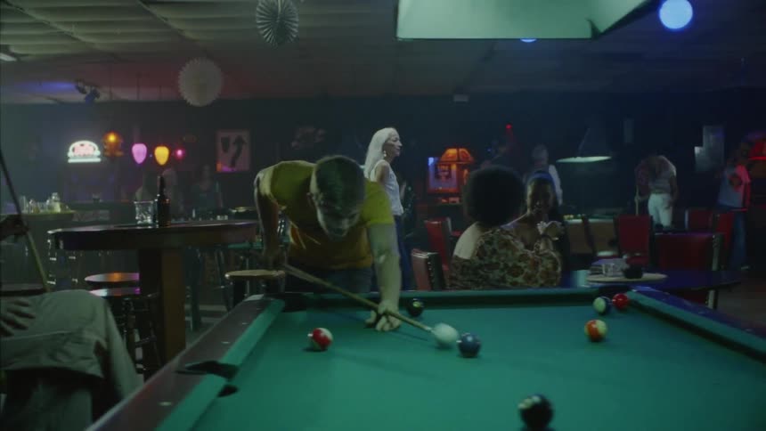 A whitehaired woman walks across a bar while other patrons play pool and eat