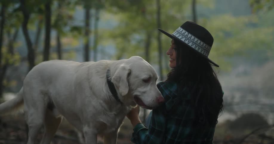 A woman pets her dog in the forest