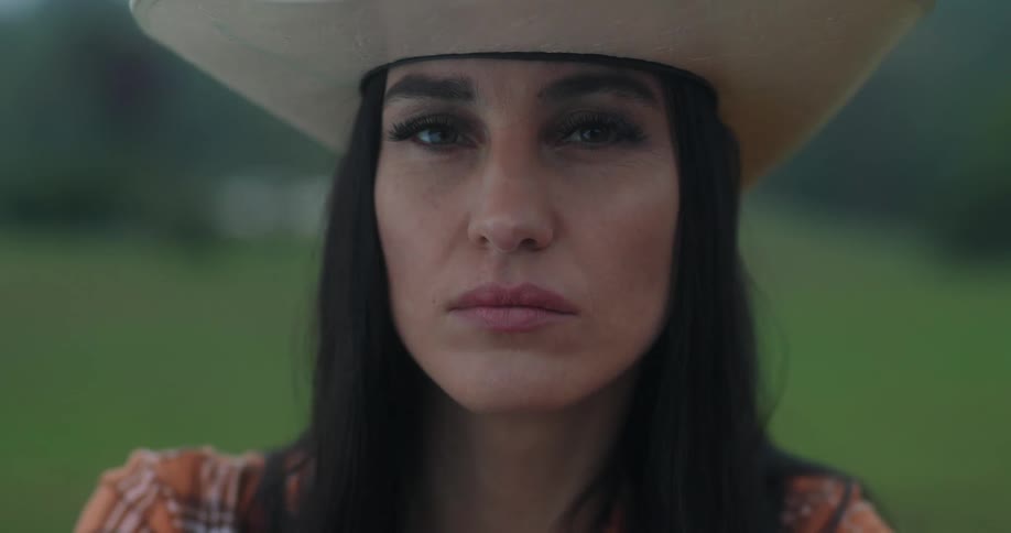 A serious woman wearing a cowboy hat staring