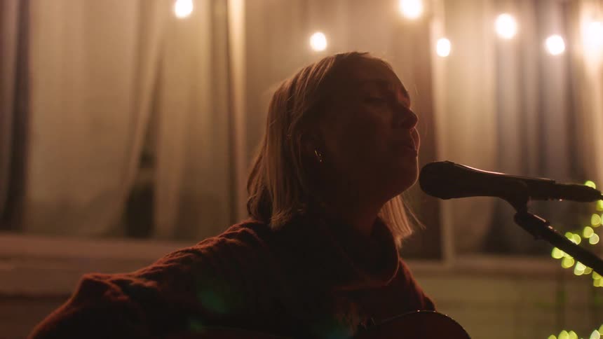 A young blonde woman is singing into a microphone while playing the guitar