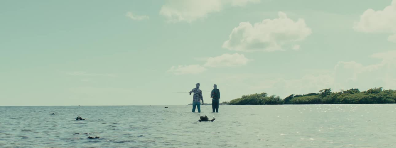 Two fishermen standing in shallow water near coast cast their fishing lines