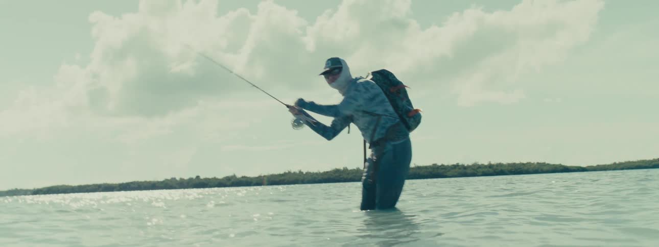 A man fishing in the ocean with the water up to his knees