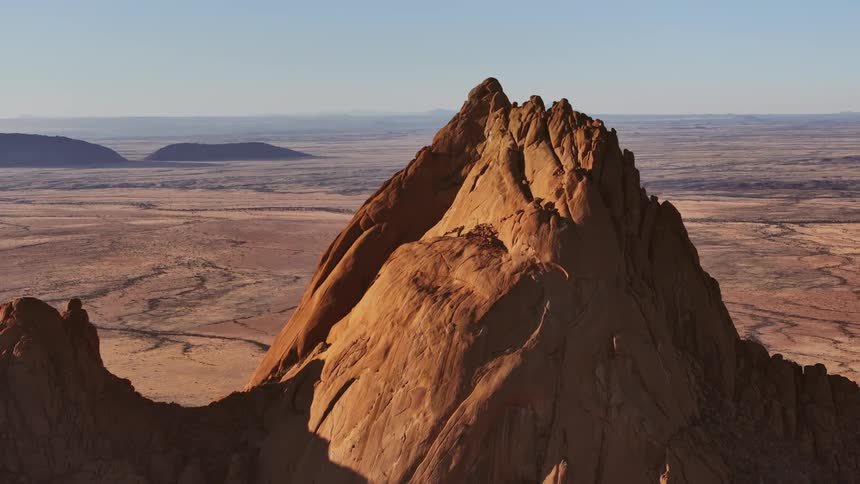 Jagged red stone mountain towers over arid flat plain