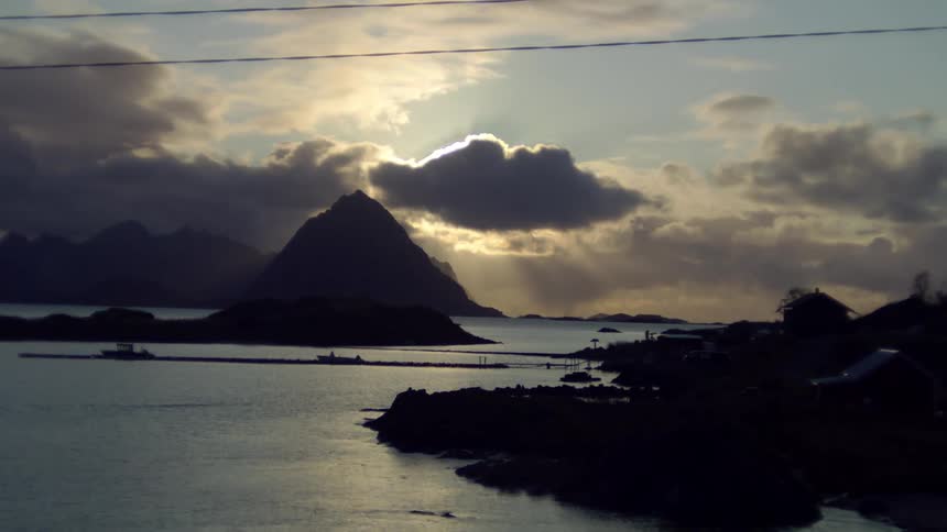 Sun sets behind clouds over coastal mountains