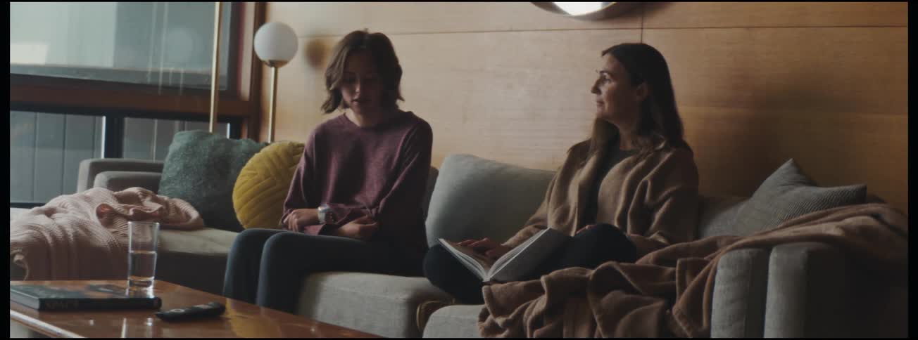 In the living room a sad daughter sits on the couch hugging her mother