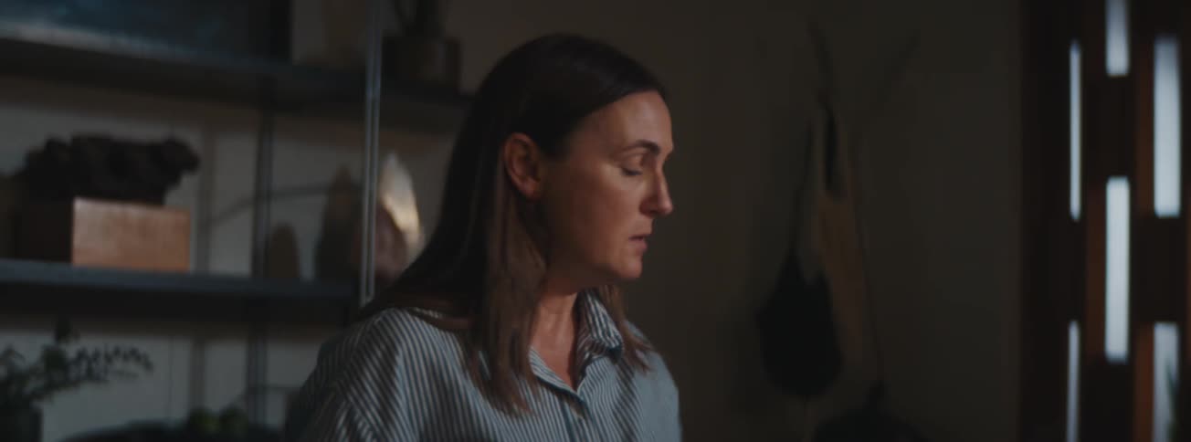 A woman sits at a desk picking up papers and looking stressed