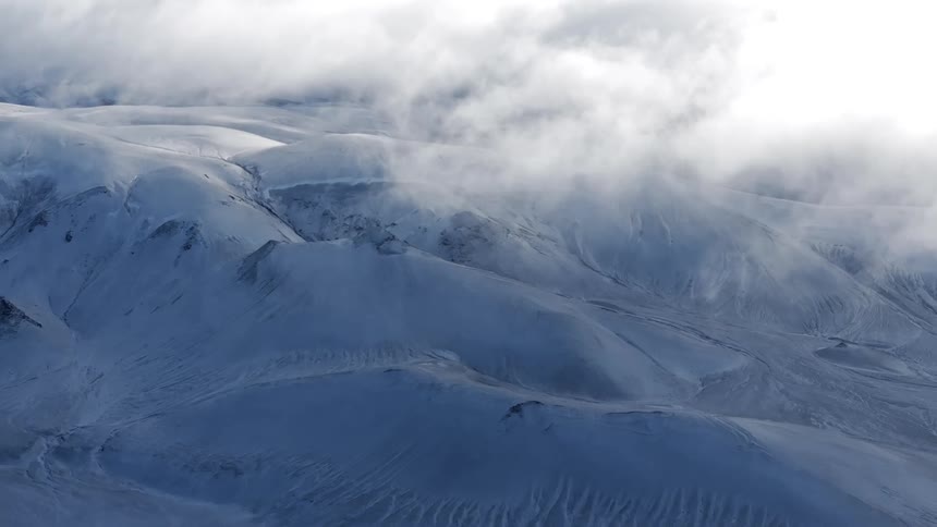 Low lying clouds partially obscure snow covered mountainous terrain