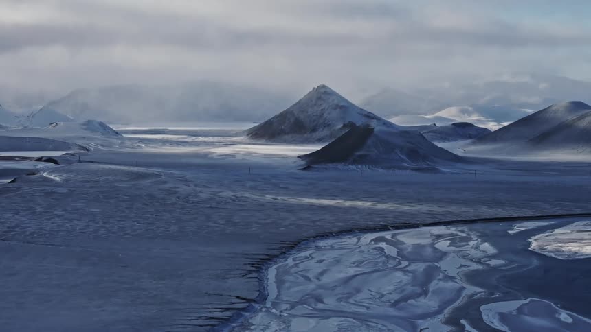 An aerial view of a freezing barren landscape of mountains and a river in the daytime