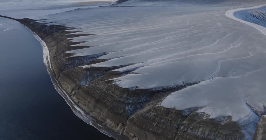 A rock formation with snow on top in front of the sea