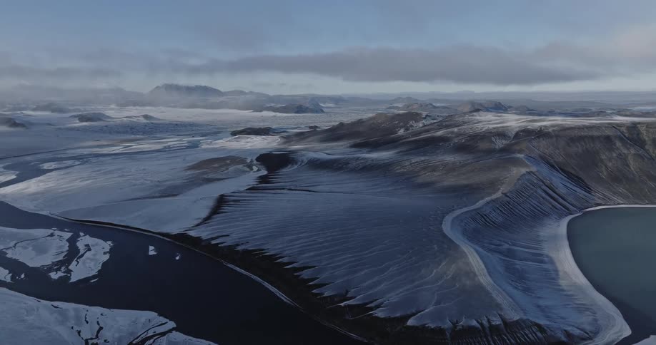 Aerial of river winding through snow covered mountainous terrain on a cloudy day