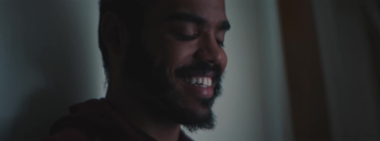 Man seated against the wall smiles while looking down indoor