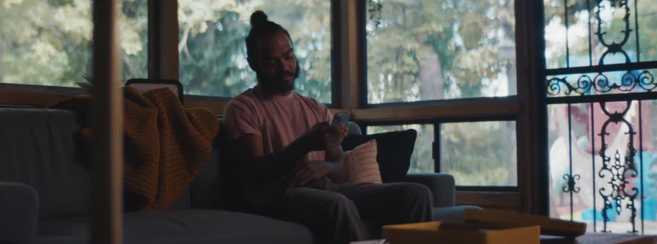 Man sitting on the living room sofa smiling while using the cellphone