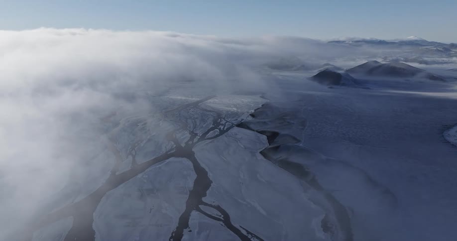 An aerial view of a frozen landscape with mountains on a cloudy day
