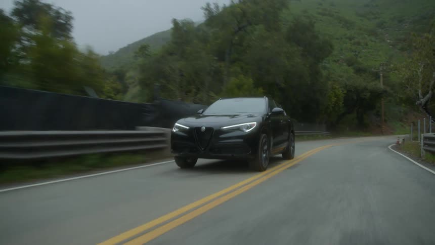 Sleek black hatchback driving quickly on a curved highway surrounded by tree covered mountain hills