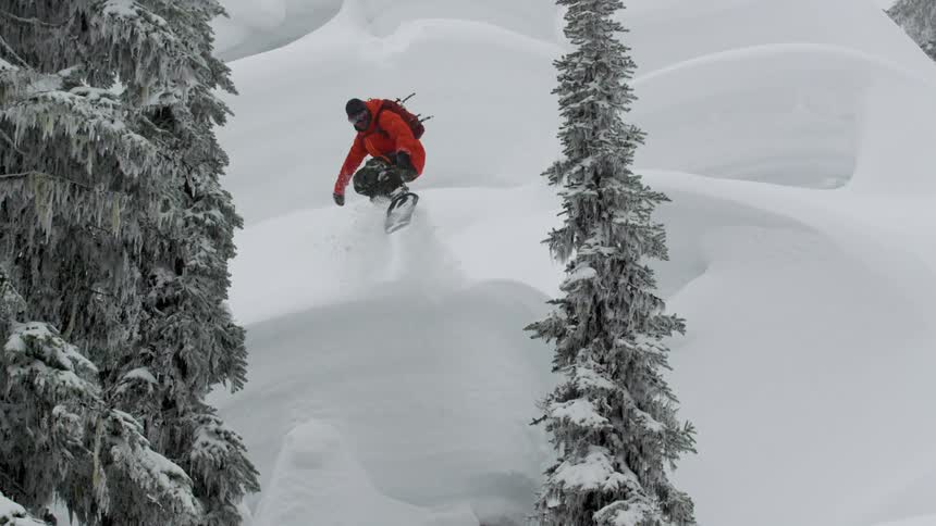 A snowboarder in the backcountry rides pillow lines in powder