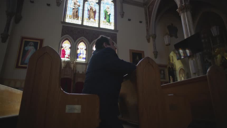 Man kneels on church pew and prays