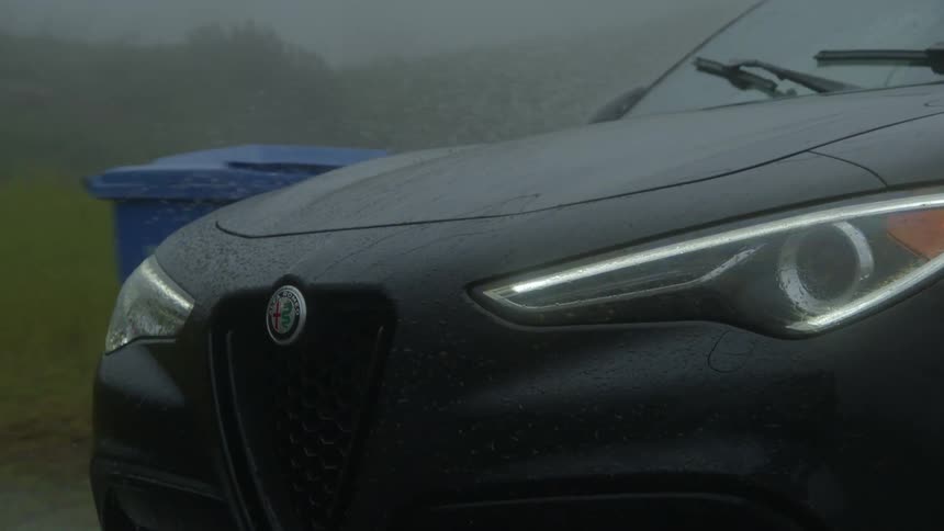 Front view of a black car driving over a puddle during rain