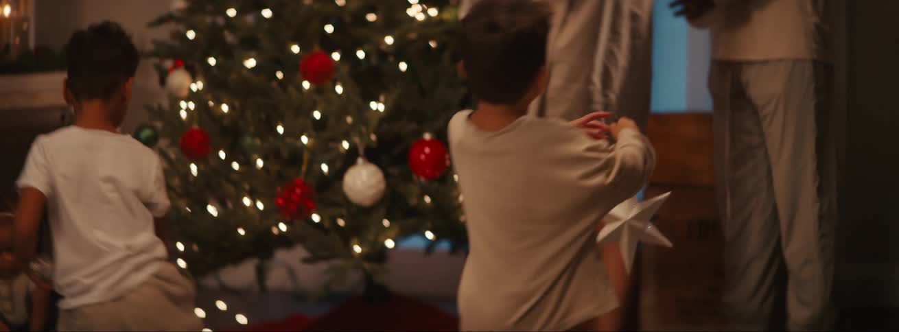 Children in a room of the house with one of them taking a christmas tree decoration star to his father