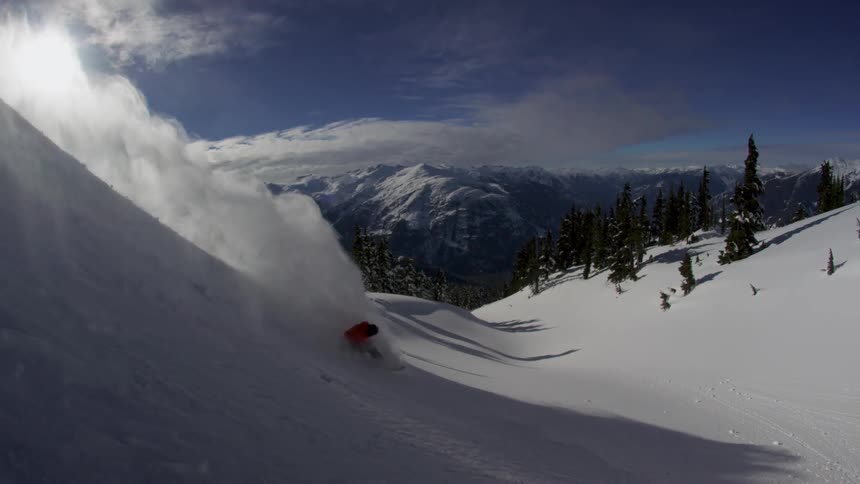 A snowboarder slashes a powdery slope on a sunny day