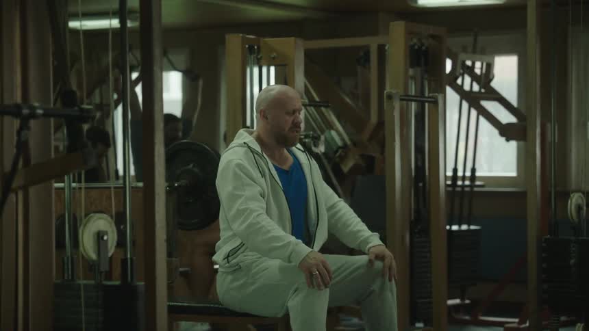 A man is sitting in a gym and has his eyes close and breathing