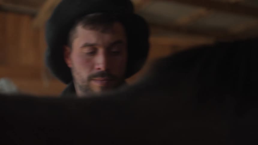 A man with a hat is running his hand through the hair of a horse that is standing still