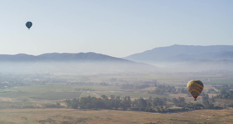 Aerial with two hot air balloons flying over the countryside with fog and mountains in the distance