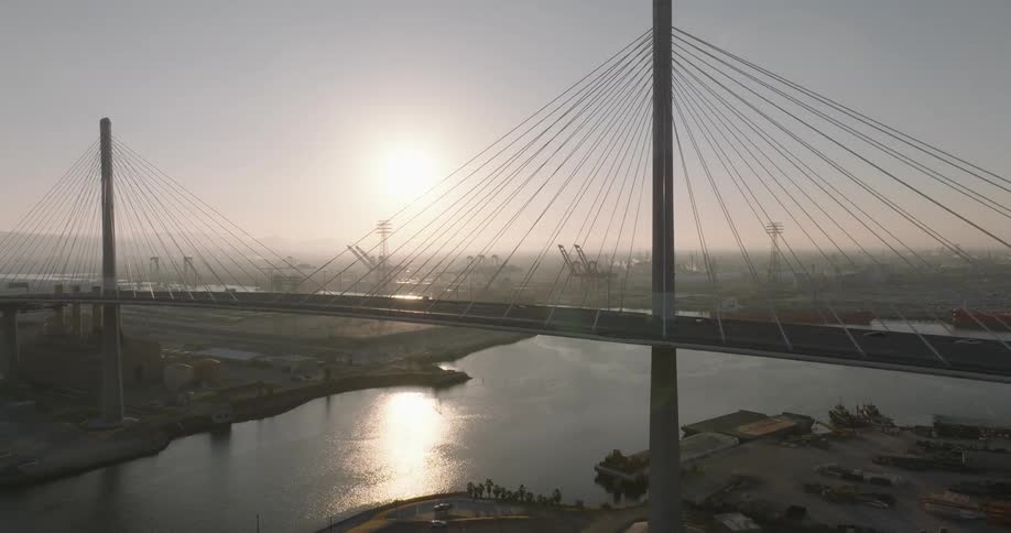 Traffic crosses bridge over river reflecting hazy sunshine with the city in the background