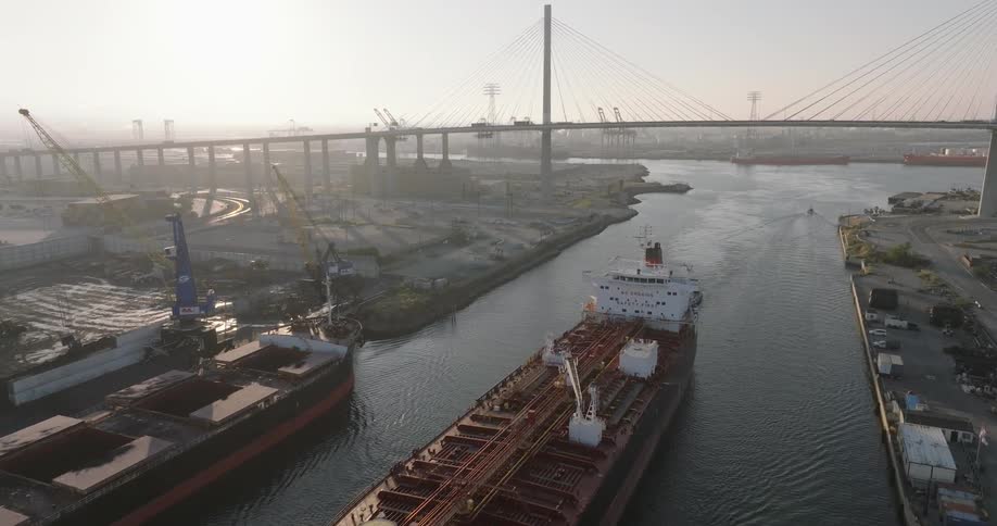 Tug boats move freighter past docks and away from busy suspension bridge on a foggy day