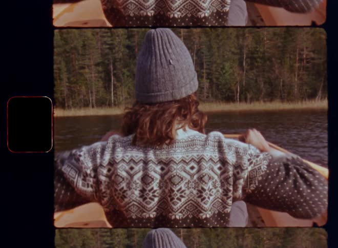 Unrecognizable male person with wide shoulders in a woollen pullover or sweater rowing or paddling a canoe or rowboat on a lake in the forest on a sunny spring time day with sun shining and a light breeze