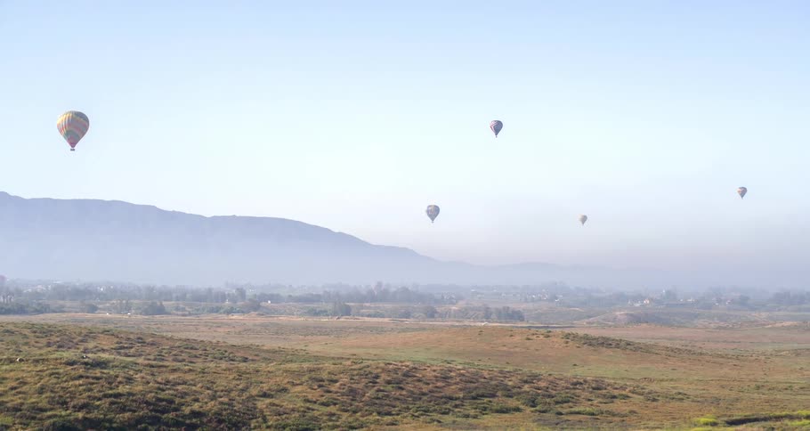 Aerial panorama of a landscape with mountains and balloons flying across the sky