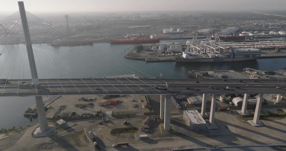 Aerial of ships in a port and traffic coming and going from bridge to land with fog and sunshine