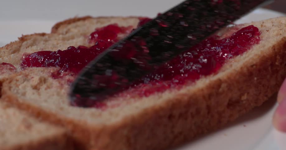 Person spreading red jam on a piece of bread