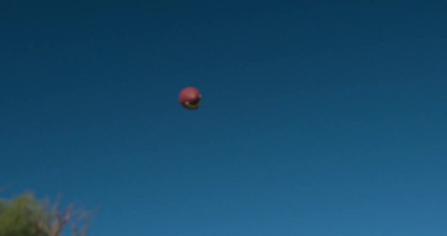 A person throws a football high into a clear sky