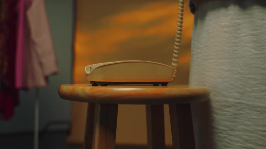 Girl answering a corded telephone on a wood stool in the middle of a room