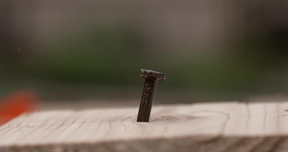 A hammer drives a nail into a board