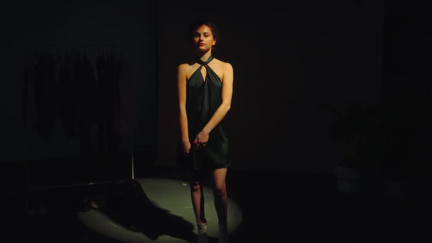 A woman in a dress is standing in the dark and is illuminated by a light